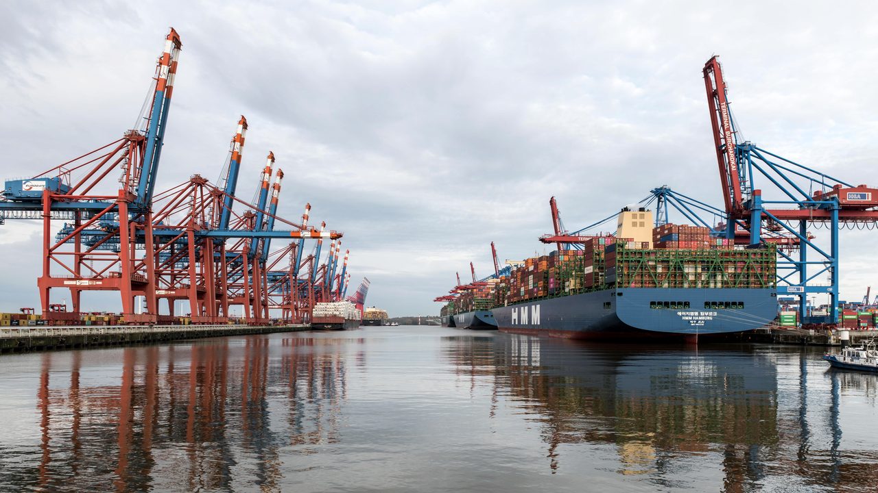 Le port de Hambourg : portiques de chargement et navires à quai, reflétés dans l'eau.