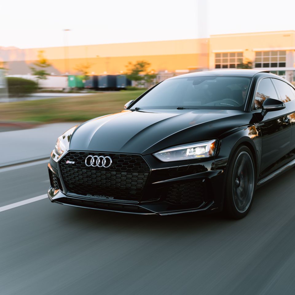 Une Audi RS5 Sportback noire roule sur une route, vue de trois quarts avant.