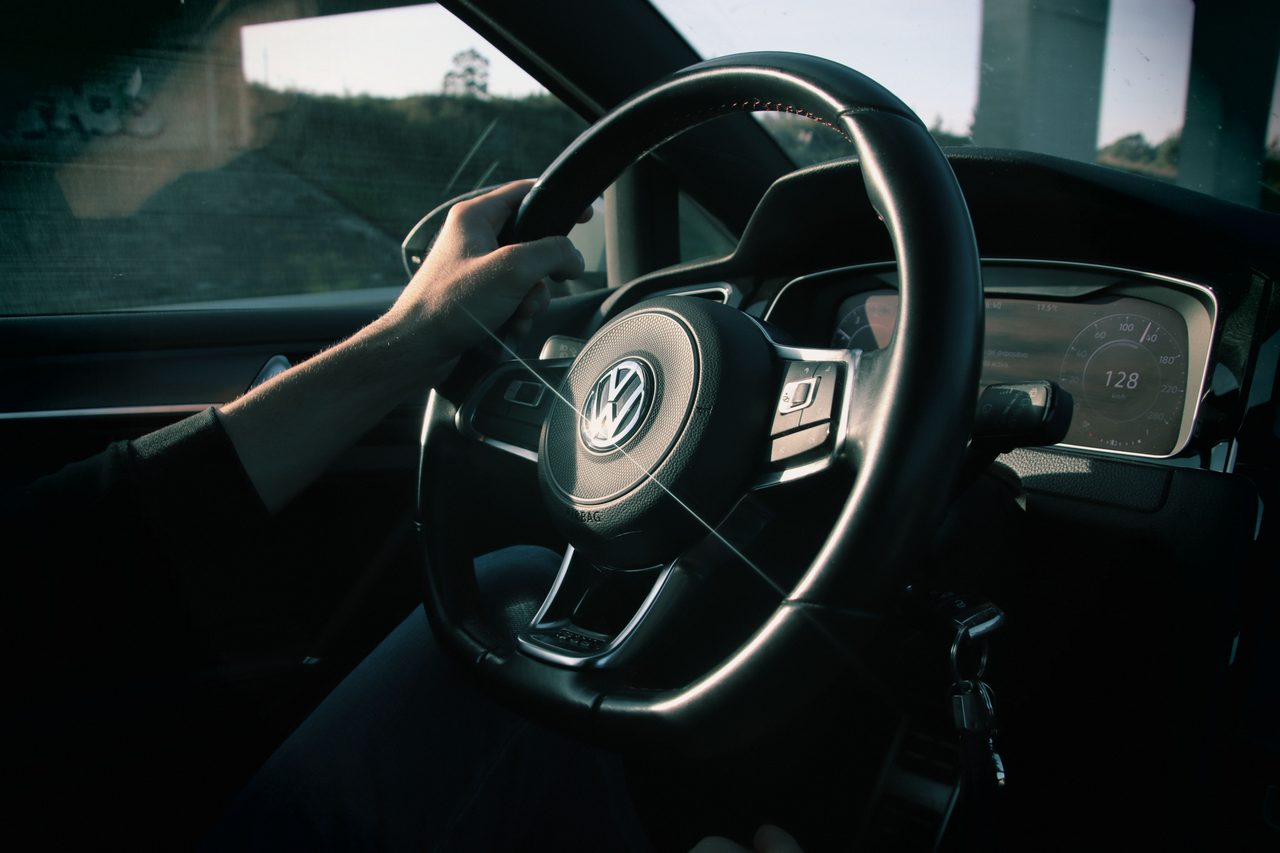 Les mains d'un conducteur sur le volant d'une Volkswagen, compteur allumé, en fin de journée.
